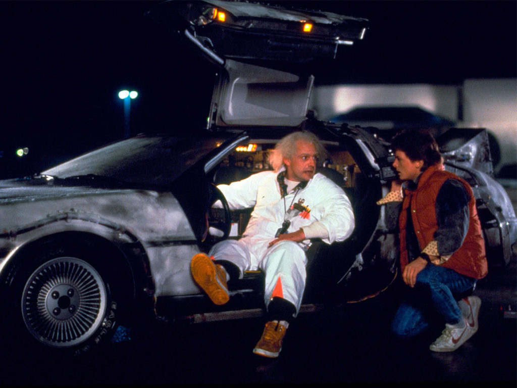 Marty McFly and Doc Brown stand beside the DeLorean time machine in Back to the Future (1985)