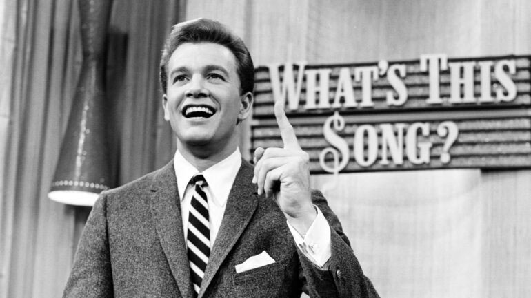 Wink Martindale in front of music trivia game show backdrop