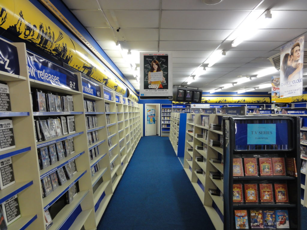 Why Blockbuster Video Became So Dominant and How It Fell - An interior shot of a vintage Blockbuster Video store showing the new releases wall lined with video cases
