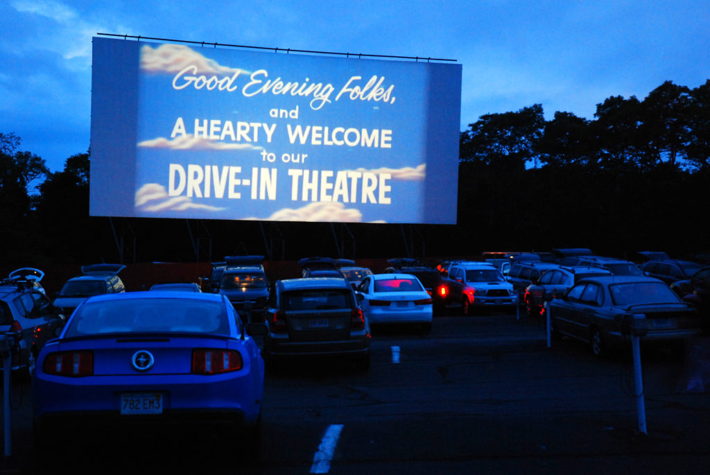 Why Drive-In Theaters Were Everywhere and Why They Vanished - A drive-in theater lot filled with cars facing a large outdoor movie projection screen
